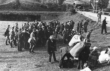 Wyrzuceni z dom&oacute;w Polacy, oczekują w punkcie zbornym na transport samochodowy (widoczny już na drugim planie) do obozu zbiorczego. Miejscowość S&oacute;l, przedpołudnie 24 września 1940 r. (fot. NSDAP; w zbiorach elektronicznych OKŚZpNP w Katowicach).